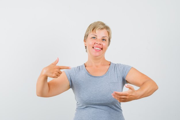 Blonde vrouw die doet alsof ze iets bij de hand houdt, wijst ernaar in een lichtblauw t-shirt en kijkt uitgeput. vooraanzicht.