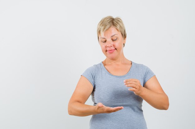 Blonde vrouw die doet alsof ze iets vasthoudt in een lichtblauw t-shirt en gefocust kijkt. vooraanzicht.