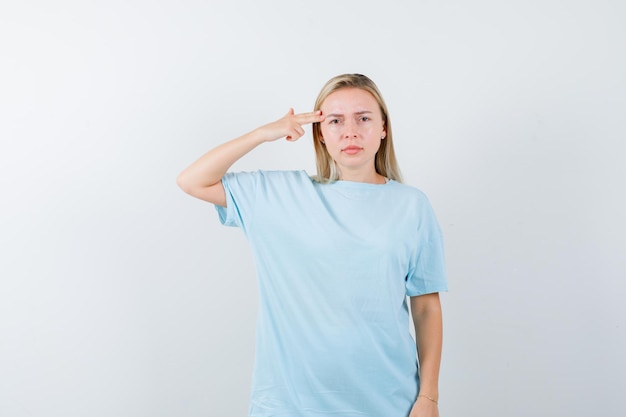 Blonde vrouw die een pistoolgebaar toont in de buurt van het hoofd in een blauw t-shirt en er serieus uitziet?