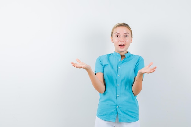 Blonde vrouw die gespreide handpalmen in blauwe blouse opheft en er verbaasd uitziet geïsoleerd