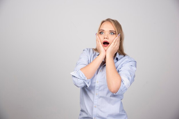 Blonde vrouw die haar gezicht vasthoudt met een verbaasde uitdrukking