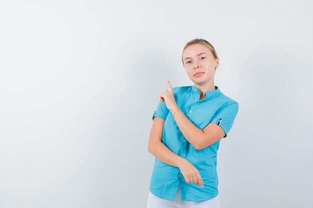 Blonde vrouw die in blauwe blouse omhoog wijst en er hoopvol geïsoleerd uitziet