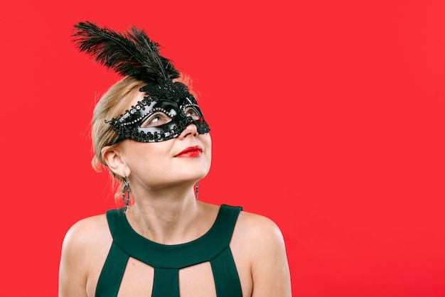 Blonde vrouw die in zwart carnaval masker omhoog kijkt