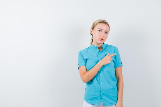 Blonde vrouw die naar rechts in blauwe blouse wijst en er serieus geïsoleerd uitziet