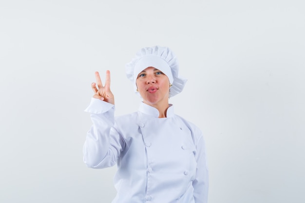 Blonde vrouw die vredesteken in witte uniforme kok toont en er mooi uitziet.