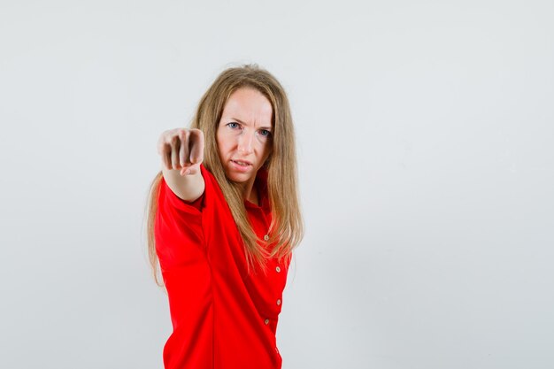 Blonde vrouw dreigt met vuist in rood shirt en woedend op zoek,