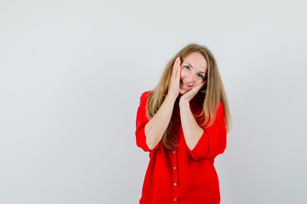 Blonde vrouw hand in hand op wangen in rood shirt en schattig op zoek.