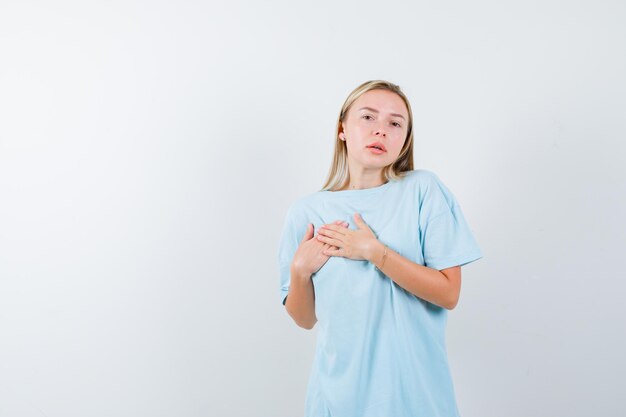 Blonde vrouw hand in hand over borst in blauw t-shirt en ziet er schattig uit