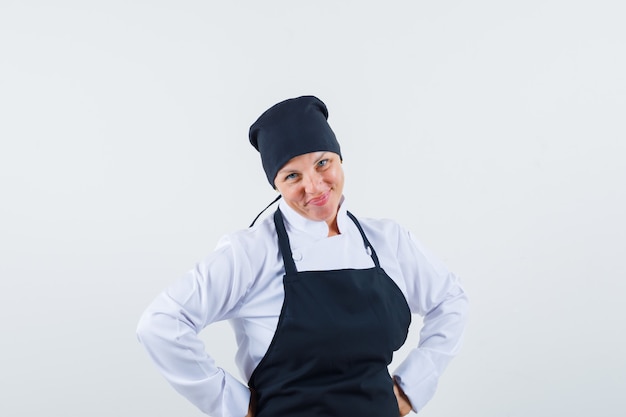 Blonde vrouw handen op taille en poseren aan de voorkant in zwarte uniform koken en er mooi uit.