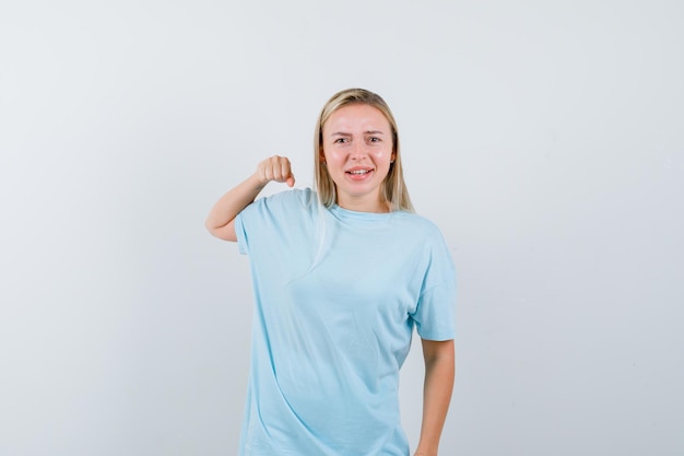 Blonde vrouw in blauw t-shirt balde vuist en ziet er zelfverzekerd uit