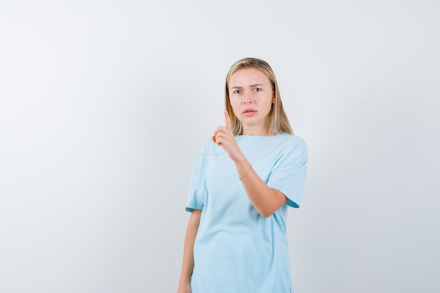 Blonde vrouw in blauw t-shirt die een klein gebaar laat zien en er serieus uitziet?