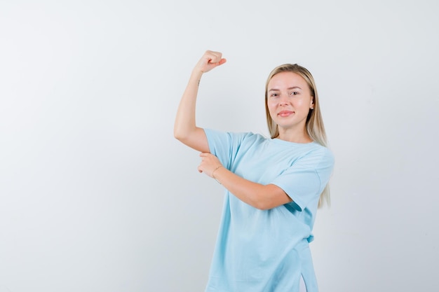 Blonde vrouw in blauw t-shirt die spieren toont en er krachtig uitziet
