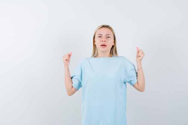 Blonde vrouw in blauw t-shirt die winnaargebaar toont en er gelukkig uitziet