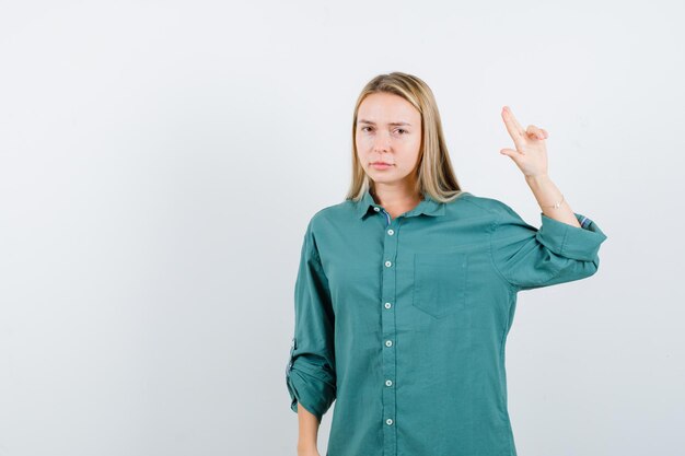 Blonde vrouw in een groen shirt die een vingerpistool maakt en er zelfverzekerd uitziet?