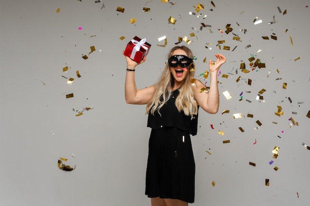 Blonde vrouw in fancy masker en jurk met cadeau.