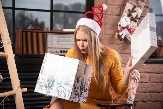 Blonde vrouw in kerstmuts op zoek binnenkant geschenkdoos.