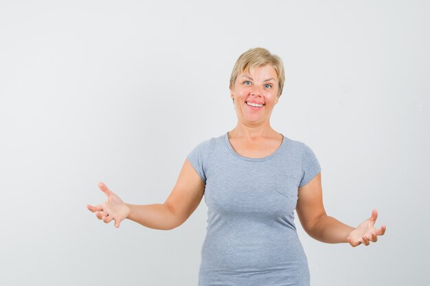 Blonde vrouw in lichtblauw t-shirt die net doet alsof ze een fles opent en gefocust, vooraanzicht kijkt.