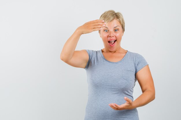 Blonde vrouw in lichtblauw t-shirt die zich als iets vasthoudt en verbaasd, vooraanzicht kijkt.