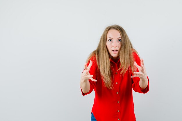 Blonde vrouw in rood shirt doet alsof ze iets grijpt en kijkt verbaasd,