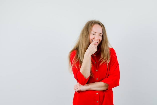 Blonde vrouw in rood shirt met vinger op mond en op zoek gelukkig,