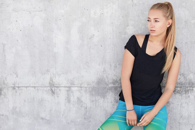 Blonde vrouw in sportkleding dichtbij betonnen muur