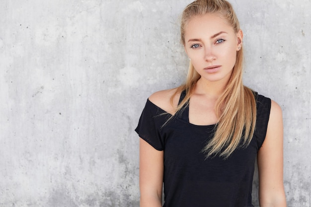 Blonde vrouw in sportkleding dichtbij betonnen muur