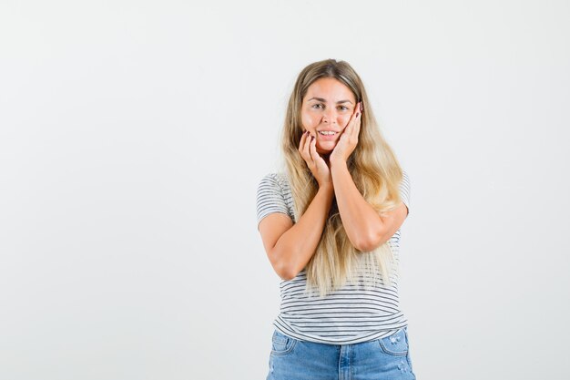 blonde vrouw in t-shirt hand in hand op haar gezicht en op zoek fris, vooraanzicht.