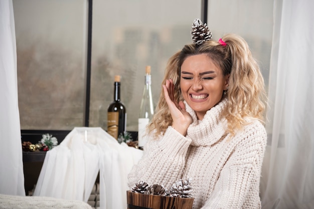 Blonde vrouw in wit sweatshirt met pinecone op haar hoofd.