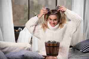 Gratis foto blonde vrouw in wit sweatshirt spelen met dennenappels.