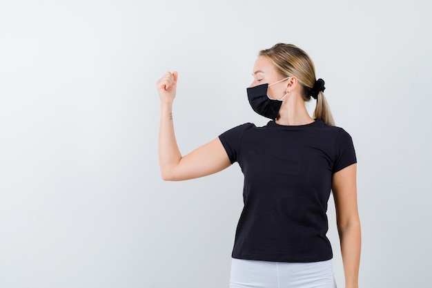 Blonde vrouw in zwart t-shirt, witte broek, zwart masker met spieren