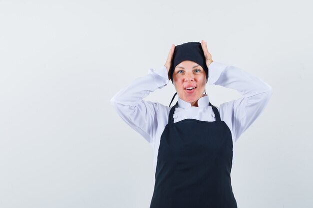 Blonde vrouw in zwarte kok uniform handen op het hoofd zetten en er mooi uitzien