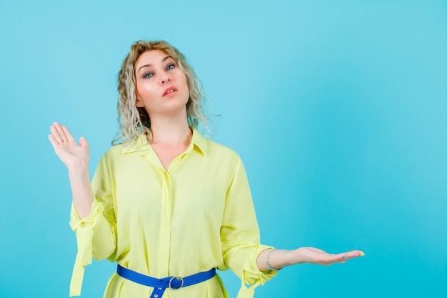 Blonde vrouw kijkt naar de camera door haar handvol op een blauwe achtergrond op te heffen