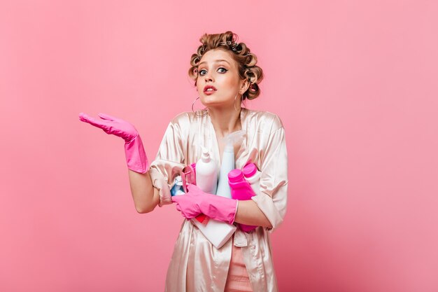 Blonde vrouw kijkt naar voren en houdt wasmiddel op roze muur