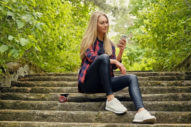 Blonde vrouw met behulp van een smartphone en zit op longboard op de trappen.