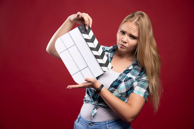 Blonde vrouw met een filmproductie klepel bord en ziet er verward en moe uit.