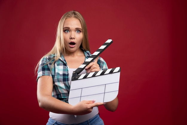 Blonde vrouw met een filmproductie klepel bord en ziet er verward en moe uit.