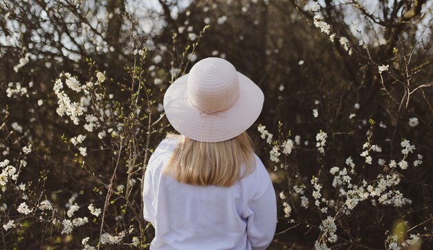 Blonde vrouw met een witte hoed met bomen op de achtergrond