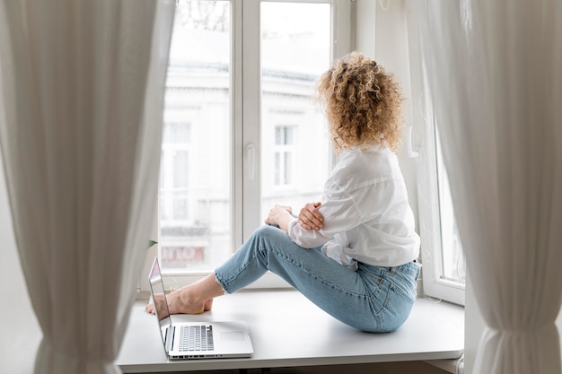 Blonde vrouw met krullend haar ontspannen thuis bij het raam