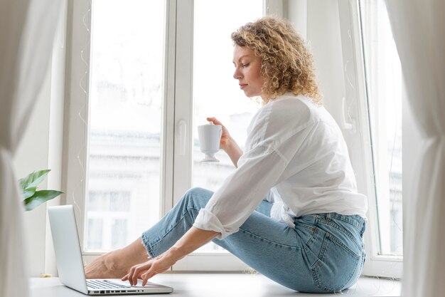 Blonde vrouw met krullend haar ontspannen thuis bij het raam