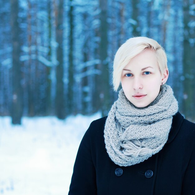 Blonde vrouw met sjaal en zwarte jas in de sneeuw