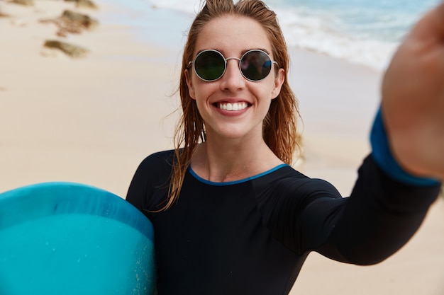 Blonde vrouw met surfplank op het strand.