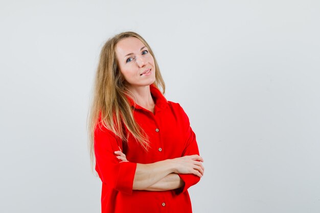 Blonde vrouw permanent met gekruiste armen in rood shirt en op zoek zelfverzekerd