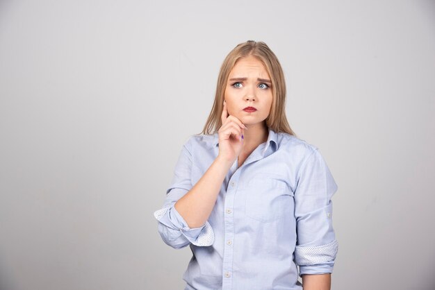 Blonde vrouw staat en kijkt serieus weg tegen de grijze muur.