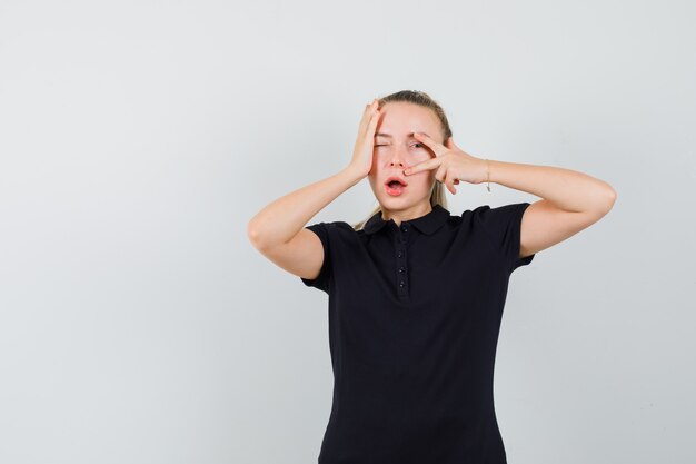 Blonde vrouw v-sign tonen en legde haar hand op het hoofd in zwart t-shirt en kijkt optimistisch