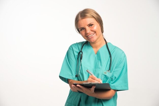 Blonde vrouwelijke arts in blauw uniform met een stethoscoop in de nek die een ontvangstbewijs schrijft.