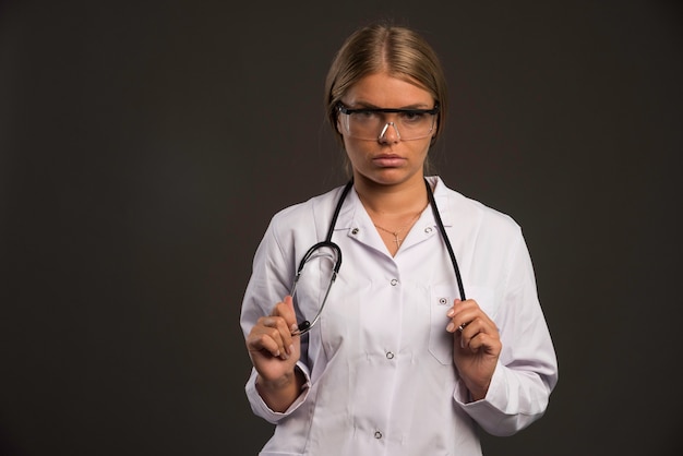 Blonde vrouwelijke arts met een stethoscoop die oogglazen draagt en recht kijkt.