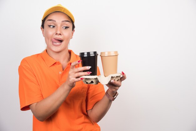 Blonde vrouwelijke koerier die twee kopjes koffie op witte muur houdt.