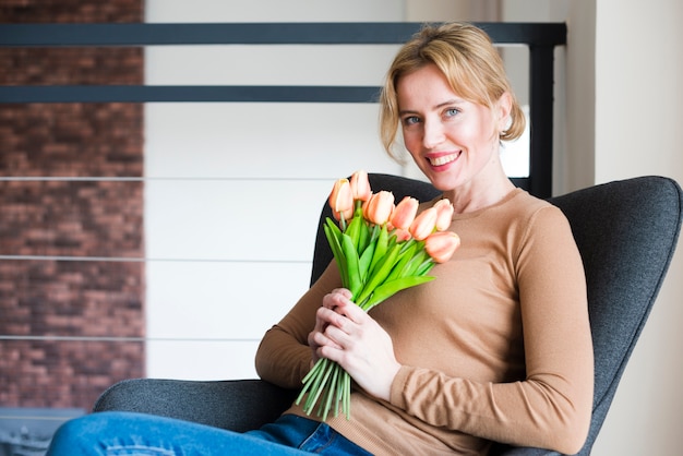 Blonde vrouwenzitting met tulpenboeket in leunstoel