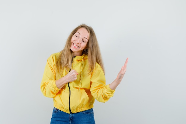 Blondedame die hand opheft en gebalde vuist in jasje, jeans en op zoek zelfverzekerd.