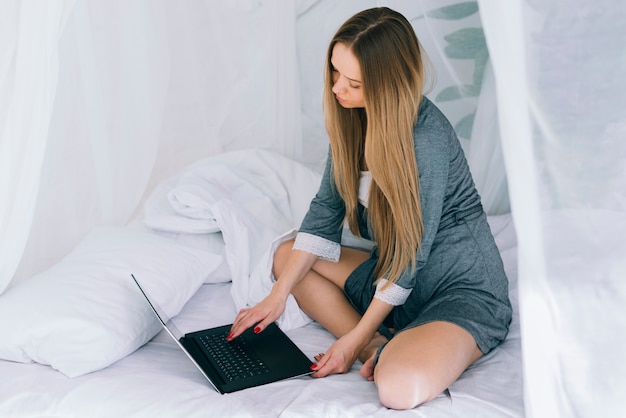 Gratis foto blondemeisje die laptop op het bed met behulp van